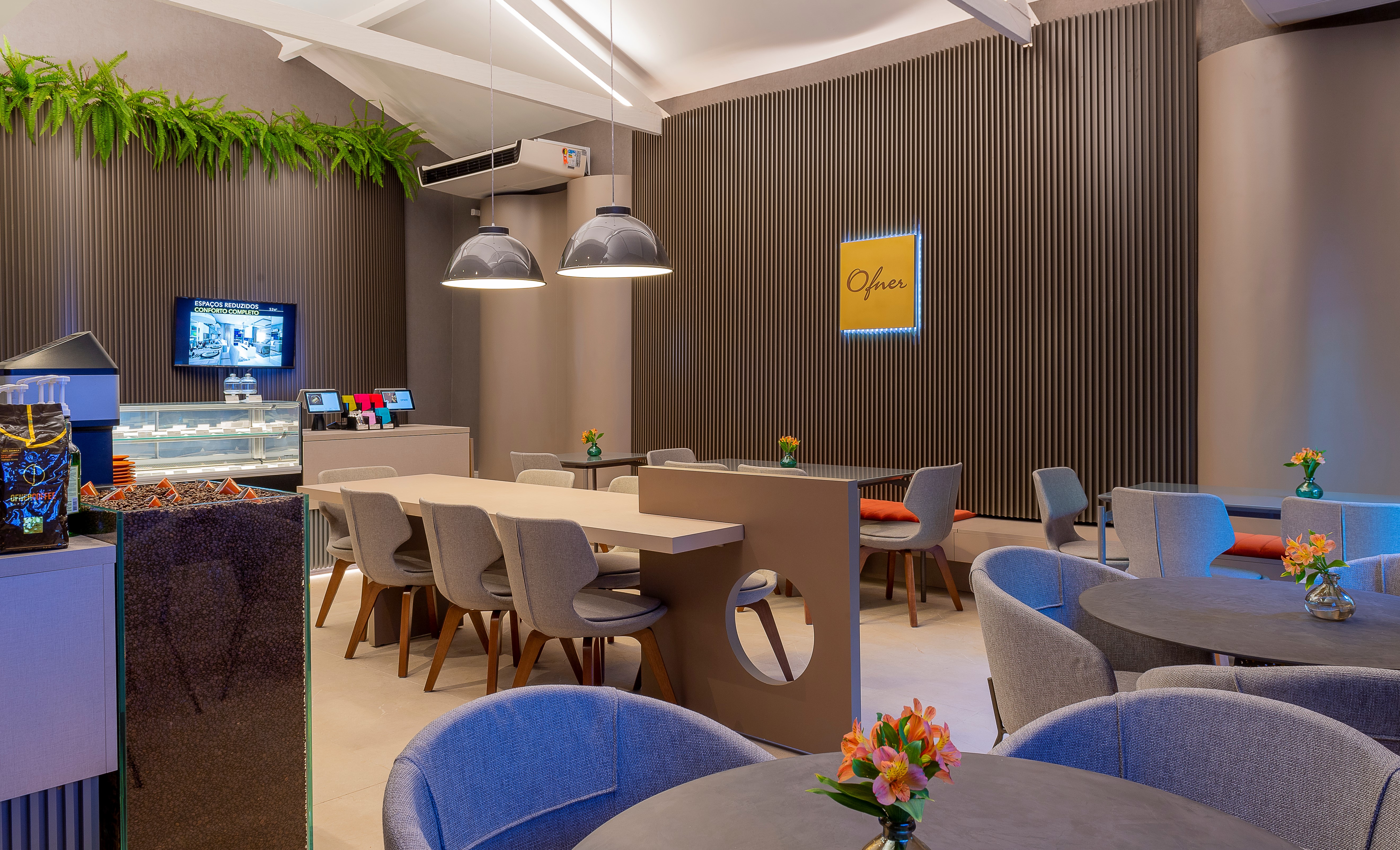 Casa Cor 2019: Um Momento Para o Café. Designer Jóia Bergamo Assina Espaço da Ofner Living da cafeteria com mesas coletivas, espaço com tons de cinza e iluminação azul.