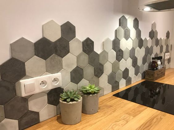 Parede com revestimento 3D. bancada da cozinha de madeira e na parede rente à ela, está os hexágonos em tons de cinza.