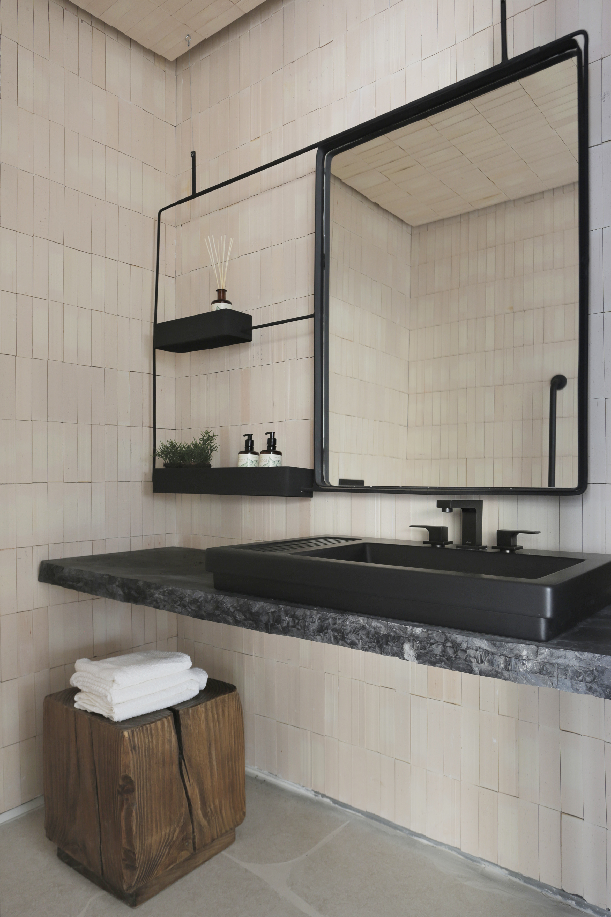 Área intima do banheiro com cuba em inox preto, espelhos com bordas pretas, mesinha em madeira natural, bancada de mármore e azulejos na cor beje.