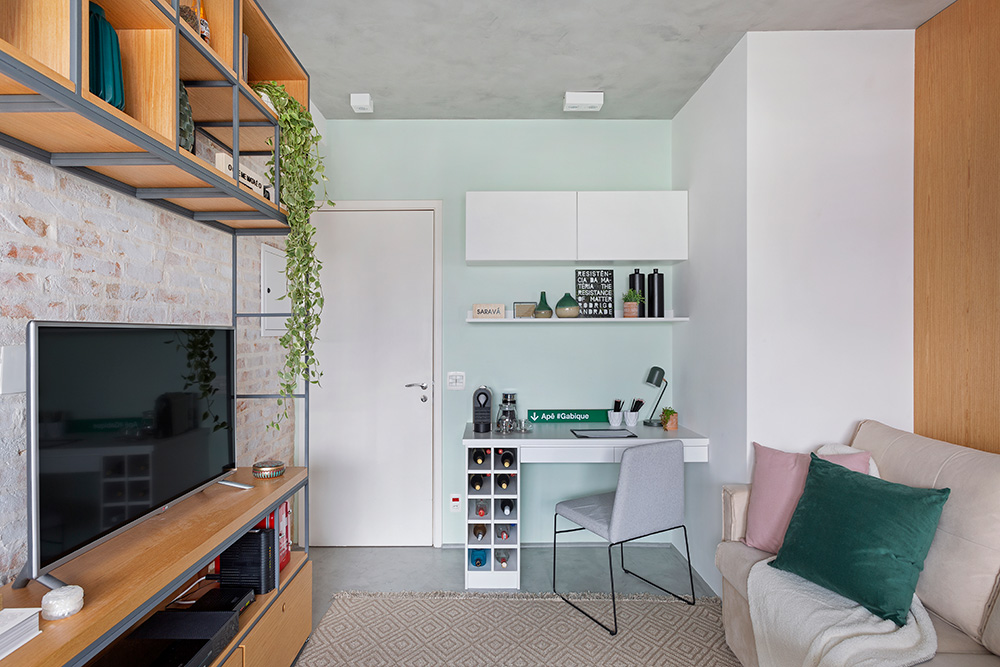 Apartamento pequeno de 35m². Parede com 3 tipos de revestimentos - madeira, tijolinho aparente e azul pastel. Estante de madeira, sofá e escrivaninha. 