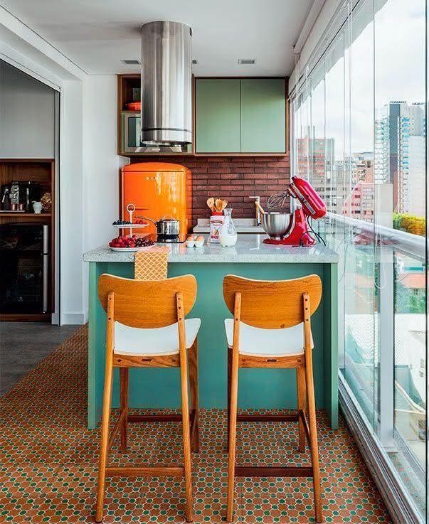 Cozinha com tapete de ladrilho hidráulico, bancada de mármore com bancos de madeira, geladeira laranja, armário verde e parede de tijolinhos.