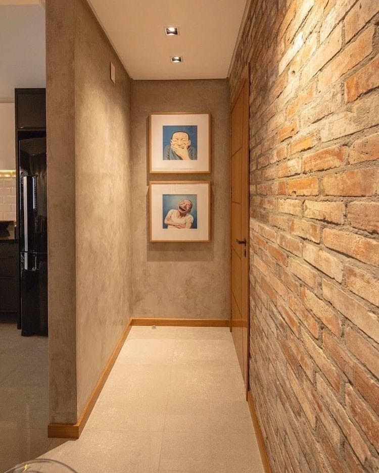 Hall de entrada de apartamento revestido com cimento queimado e outra parede de tijolinhos, com quadros para compor a decoração 