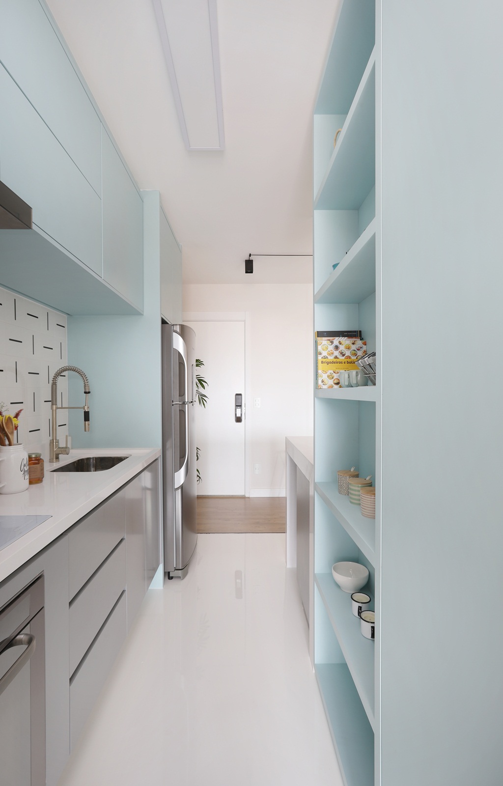Cozinha de apartamento com armário azul, porcelanato branco e pia branca e azulejo preto e branco