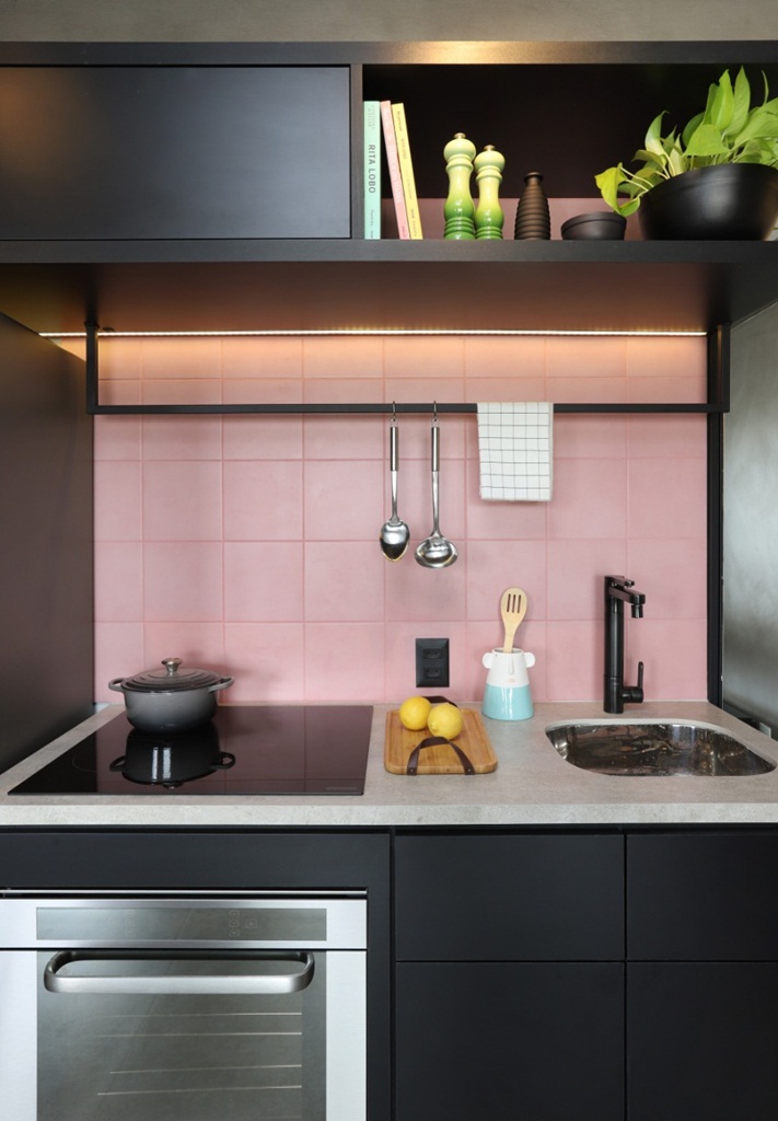 Panela sobre cooktop, bancada de porcelanato, com torneira preta e azulejo rosa.