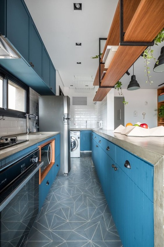 Cozinha pequena com área de serviço, armários azuis, piso geométrico e azulejo subway branco.