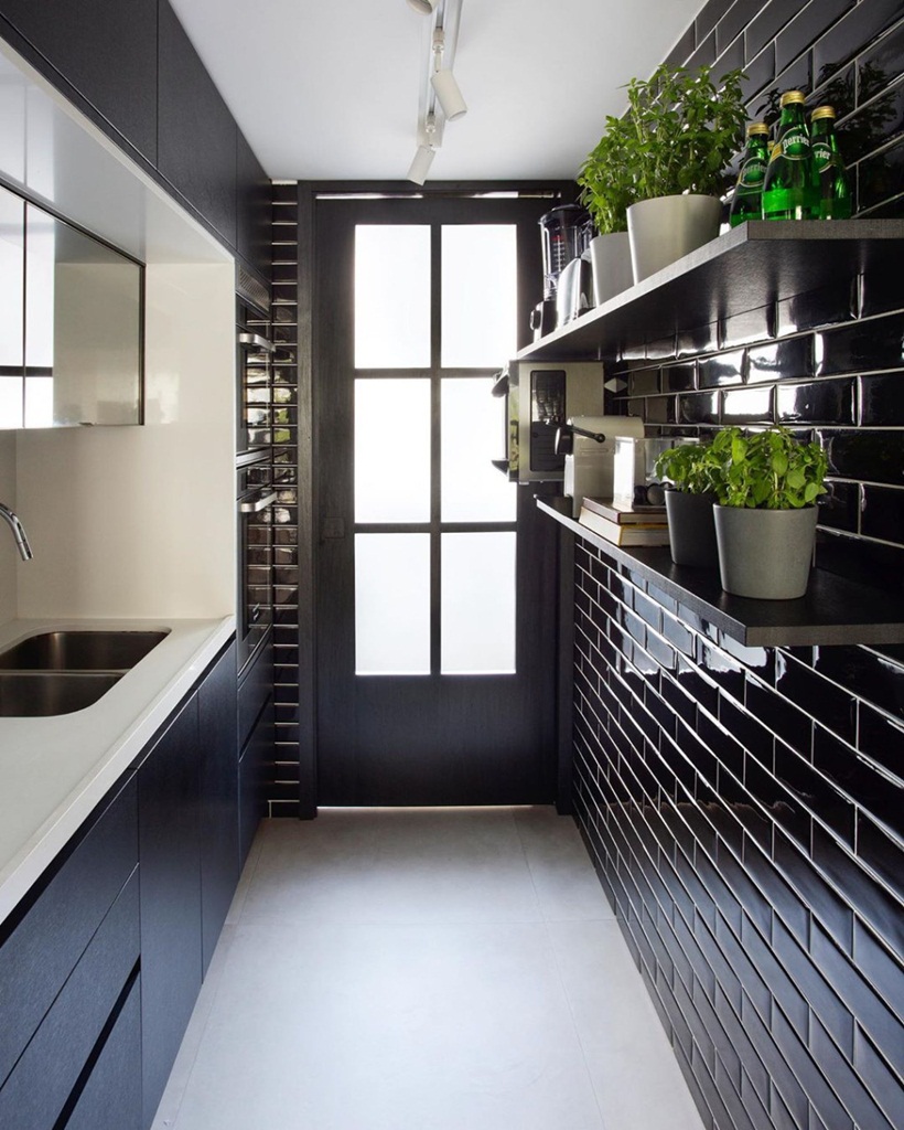 Cozinha pequena com azulejos preto, prateleiras com vazos de flor, armário preto e bancada da pia branca.