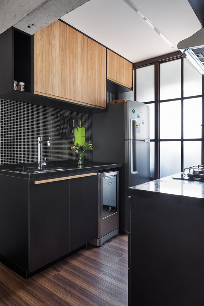Cozinha com piso de madeira, armários pretos e marrom, geladeira cinza e pastilhas pretas na parede.