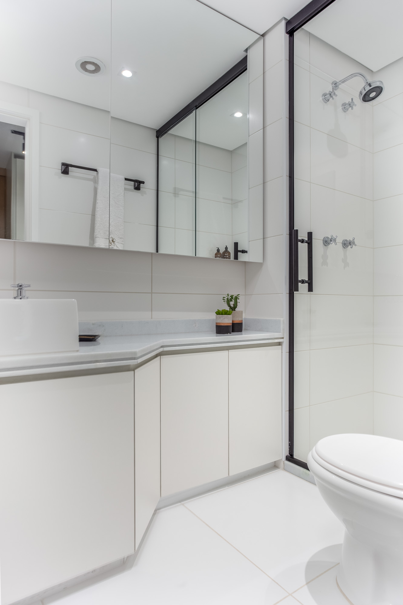 banheiro com armário, piso e azulejo branco, box de vidro com detalhes preto.
