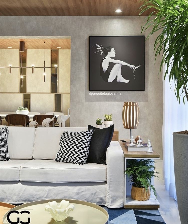 Sala com sofá branco, almofadas preta e branca, plantas, mesinha de centro e quadro decorativo.
