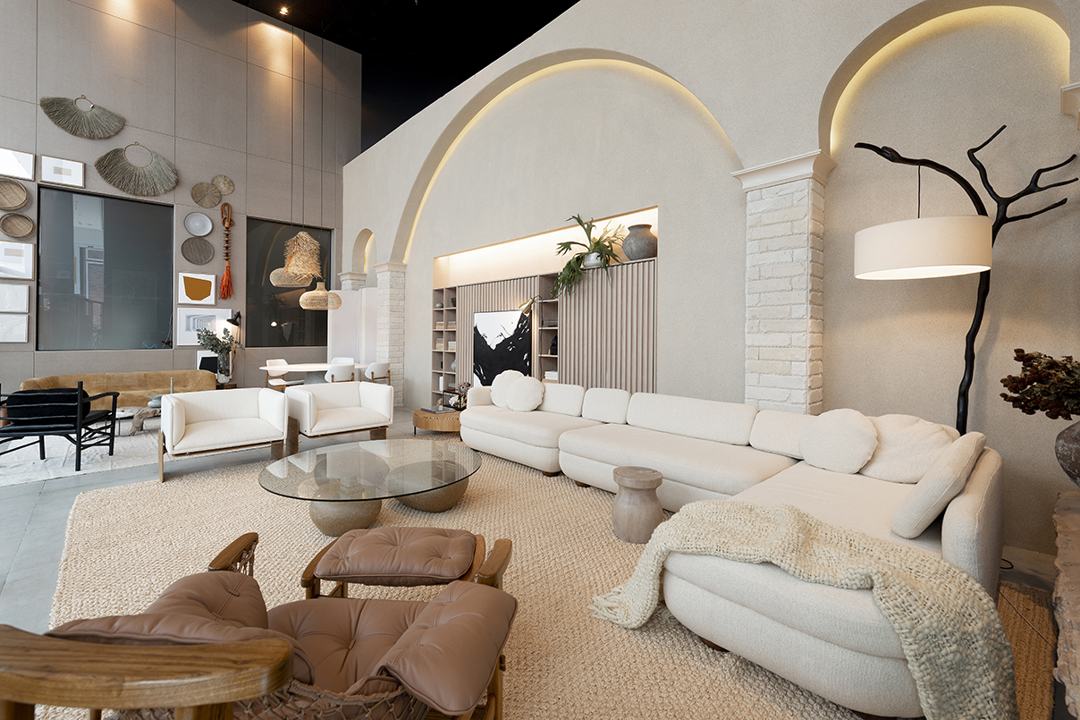 Janelas CASACOR - ambiente com sofás e poltronas brancas, mesinha de centro redonda de vidro, paredes brancas com luminárias pendentes e tapete bege.
