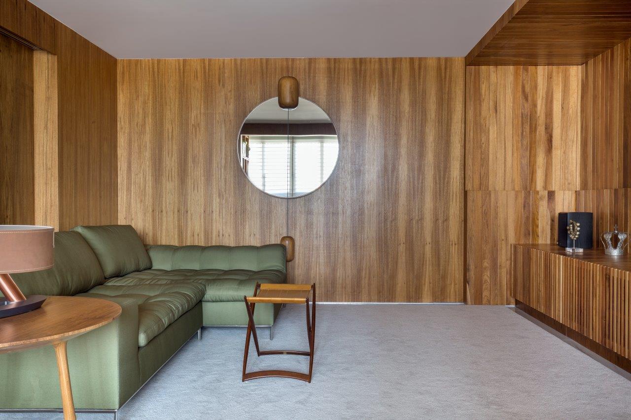 Sala de descanso com marcenaria em tom natural por toda a sala, sofá verde e piso cinza.