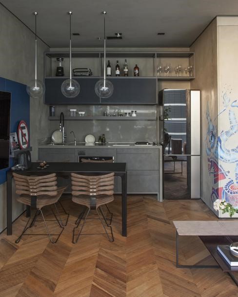 Cozinha com armários cinza, mesa preta de 4 lugares com cadeiras marrom, piso de madeira e lâmpadas pendentes.
