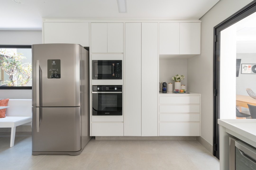 Cozinha com armários brancos, geladeira de inox e piso em tom neutro