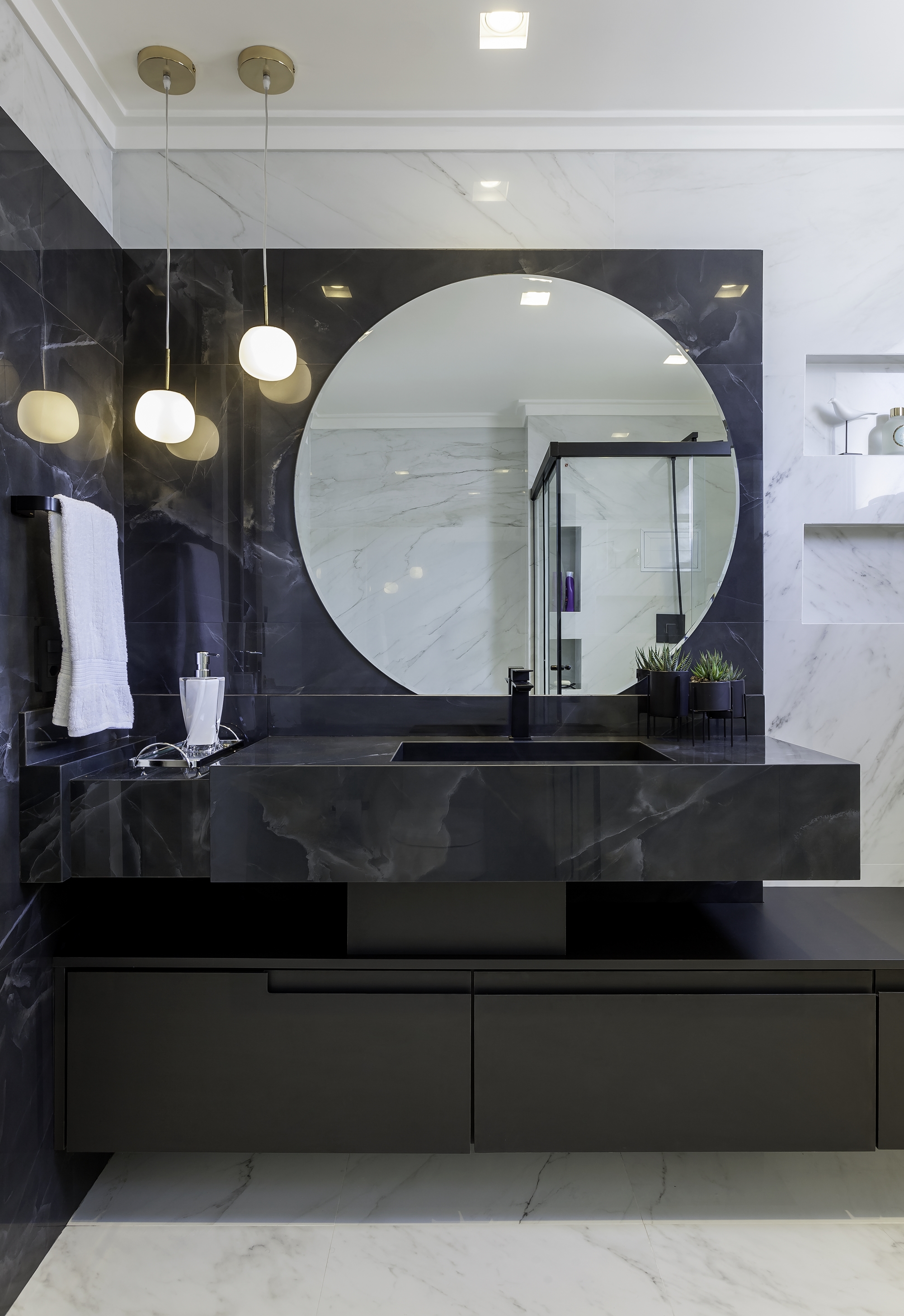 Banheiro com decoração com personalidade com mármore preto aplicado na parede da pia e pia, revestimento branco  aplicado nas demais paredes, piso porcelanato branco e armários em tom grafite