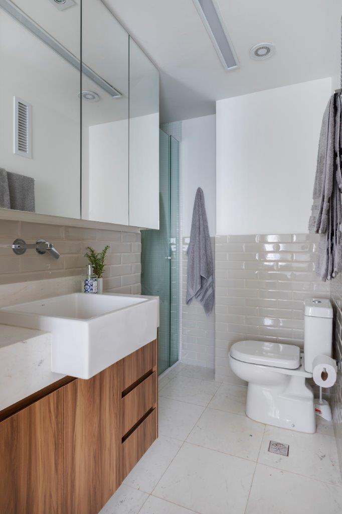 Banheiro com piso branco, parede com técnica de pintura de meia parede branca e outra metade com azulejo subway tile branco, gabinete de madeira com cuba branca.