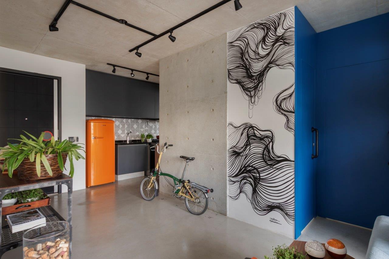 Hall de entrada com piso porcelanato em tom neutro, parede de cimento queimado com bicicleta encostada, parede com arte personalizada em preto e branco e vista da parede azul da sala.