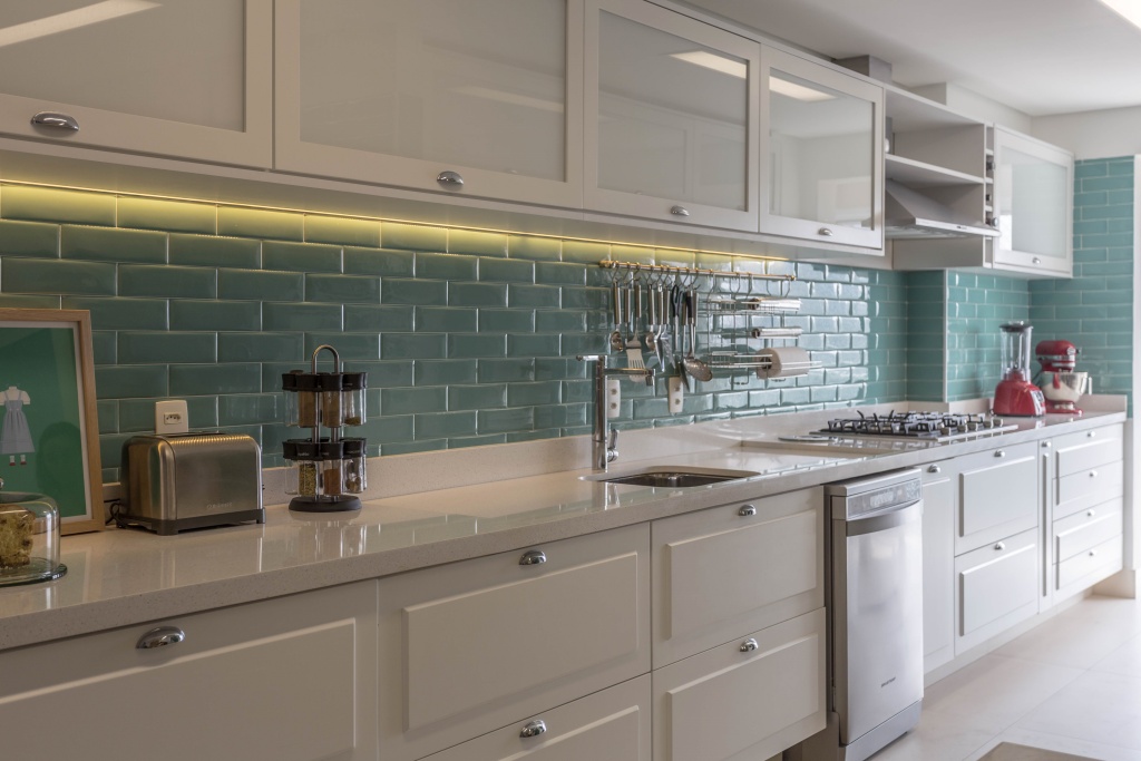 cozinha com paredes revestidas com azulejo subway tiles verde claro muito sutil, armários branco clássico com moldura  e piso liso branco.