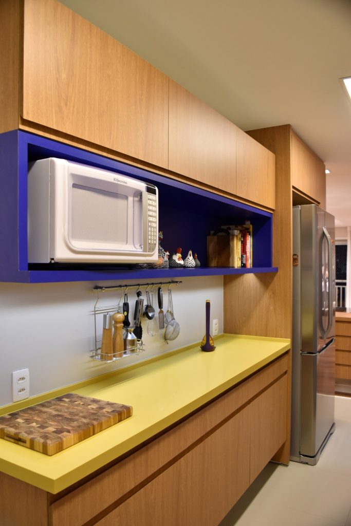 cozinha com armário amadeirado com bancada amarela e nicho azul, piso neutro e parede branca.