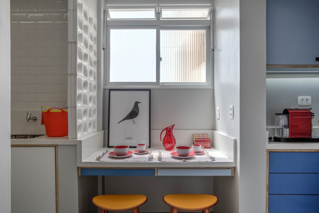 cozinha com armários azul e branco, paredes brancas, bancos amarelos e utensílios vermelho e laranja.
