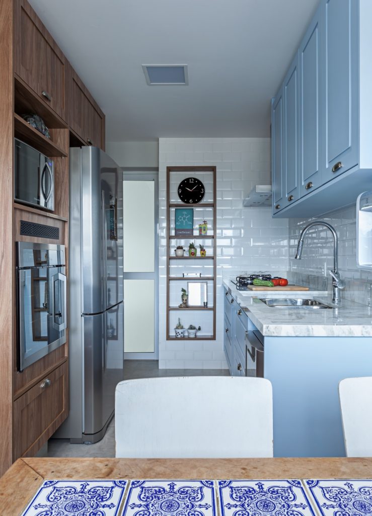cozinha em estilo retro com azulejo subway tiles branco, armários azuis e marrom escuro, eletrodomésticos de inox, mesa de madeira e piso de cimento queimadp