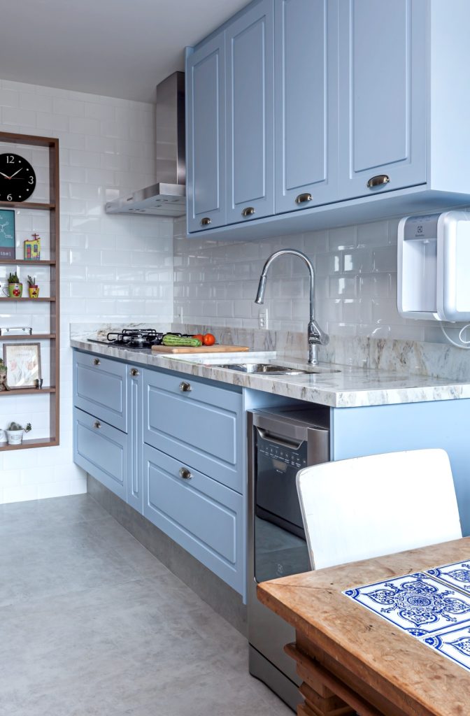 cozinha em estilo retro com azulejo subway tiles branco, armário azul, eletrodomésticos de inox, mesa de madeira com cadeira branca e piso de cimento queimado
