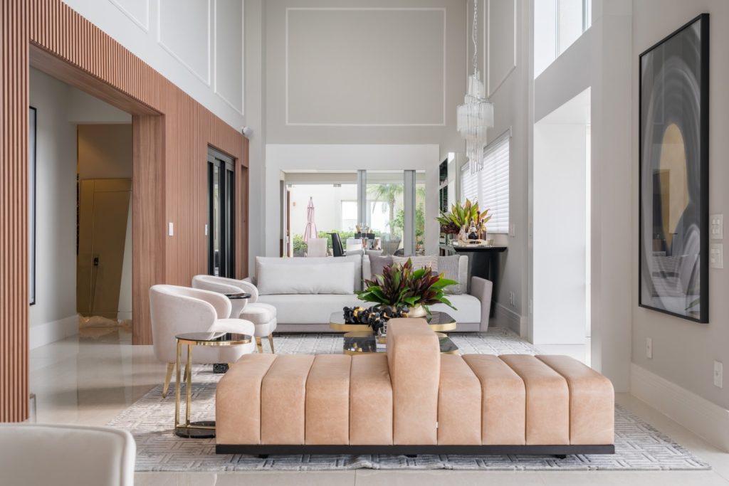 reforma de apartamento - sala de estar com sofá e poltronas brancas, piso porcelanato branco, paredes brancas, uma parede lateral com madeira ripada integrada a adega.