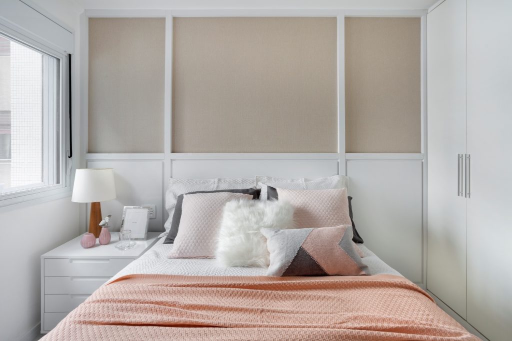 Quarto com o branco sendo a cor predominante com pontos de bege na parede, rosa no jogo de cama, e o cinza evidenciados na manta e almofadas