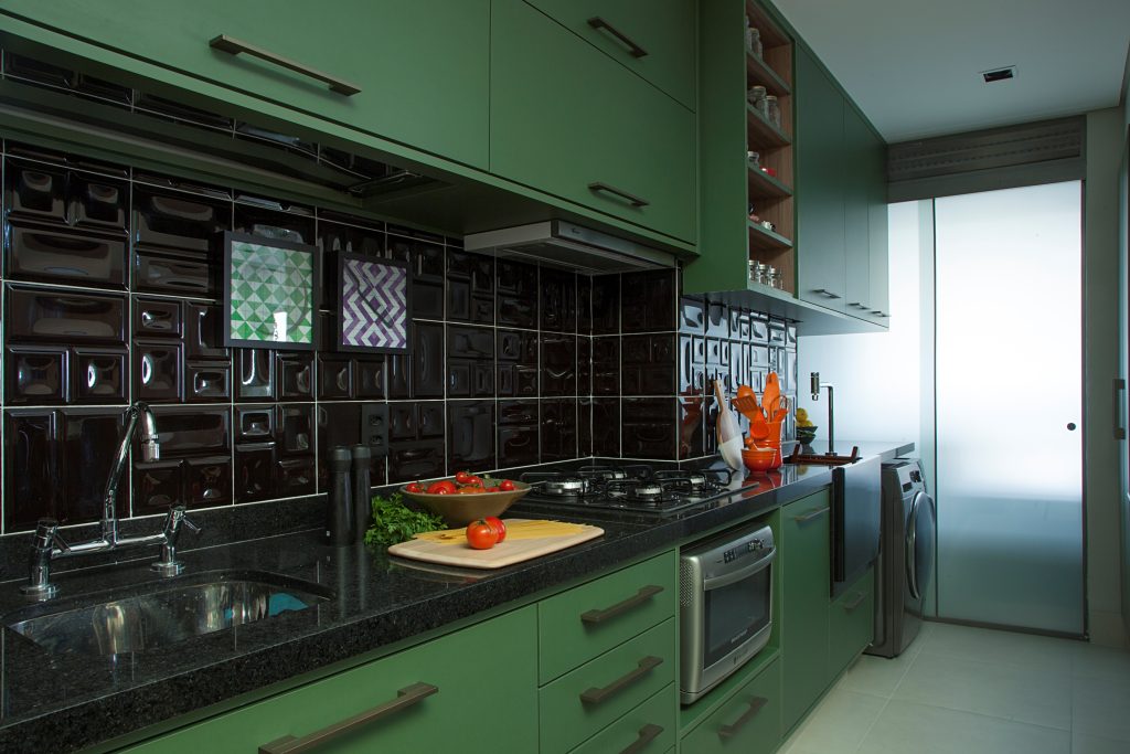 Cozinha com armário verde, bancada da pia de mármore preto, azulejo preto na parede da pia e piso em tom neutro
