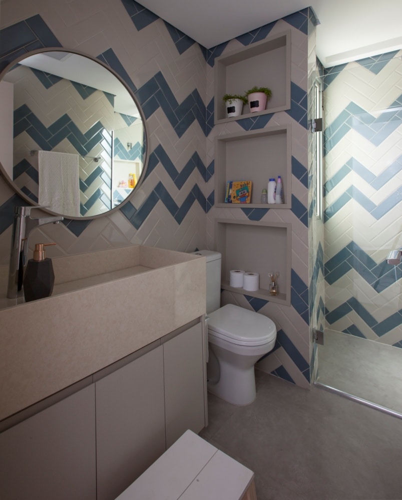 Banheiro com azulejos azul e branco em formato zig zag, piso de cimento queimado, cuba e pia em tom neutro
