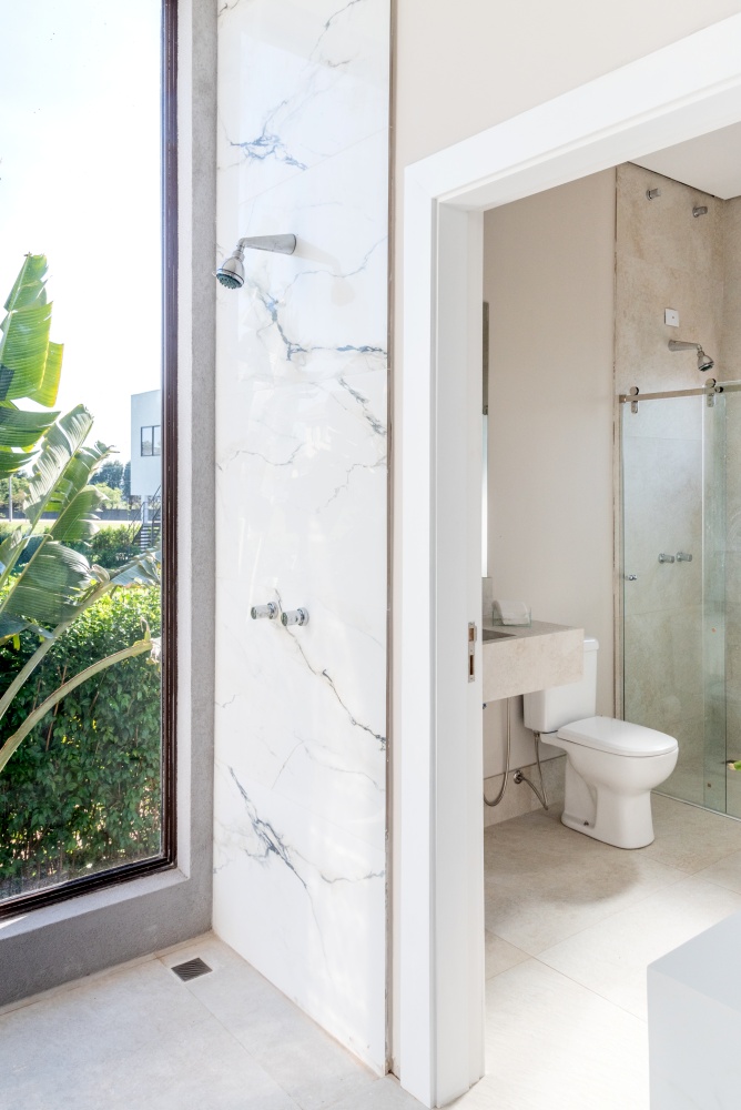 Banheiro com ducha para utilização pós sauna , com pia revestida de porcelanato marmorizado branco, piso em tom neutro e vasos decorativos no chão