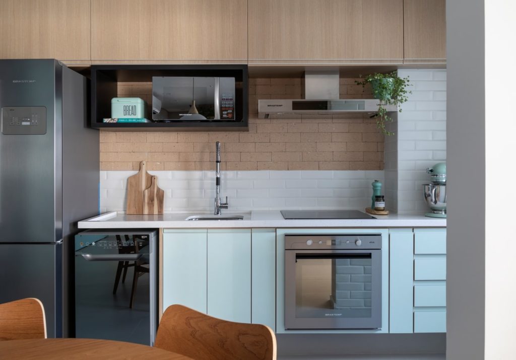 Cozinha com parede de tijolinhos branco e tom neutro, armários em tom neutro e mesa redonda de madeira.