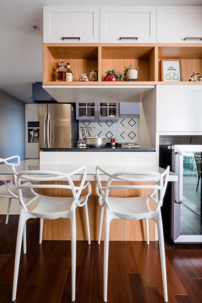 cozinha com ilha e bancada: cozinha de apartamento com bancada pequena com duas cadeiras brancas e piso de madeiras 