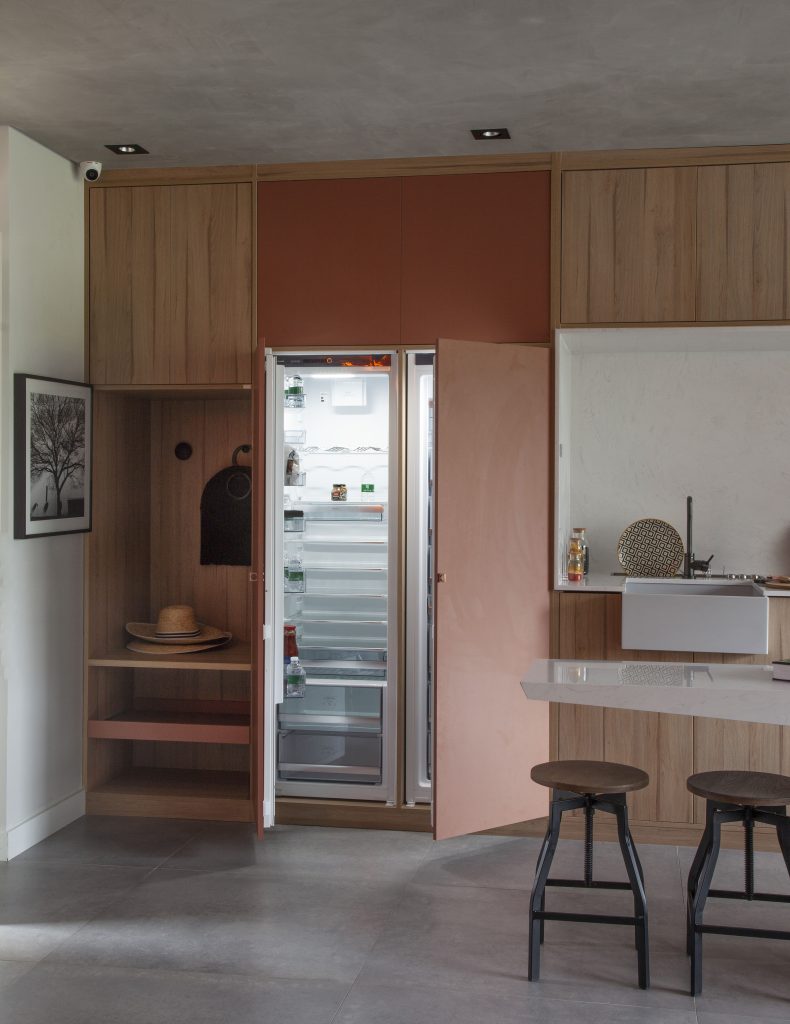 Armário da cozinha marrom com porta laranja, atrás da porta tem uma geladeira oculta