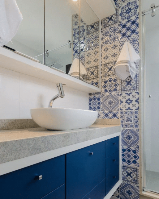 Banheiro com ladrilho hidraulico azul e branco na lateral da parede, armário com porta azul, azulejo branco na parede da pia e cuba branca.