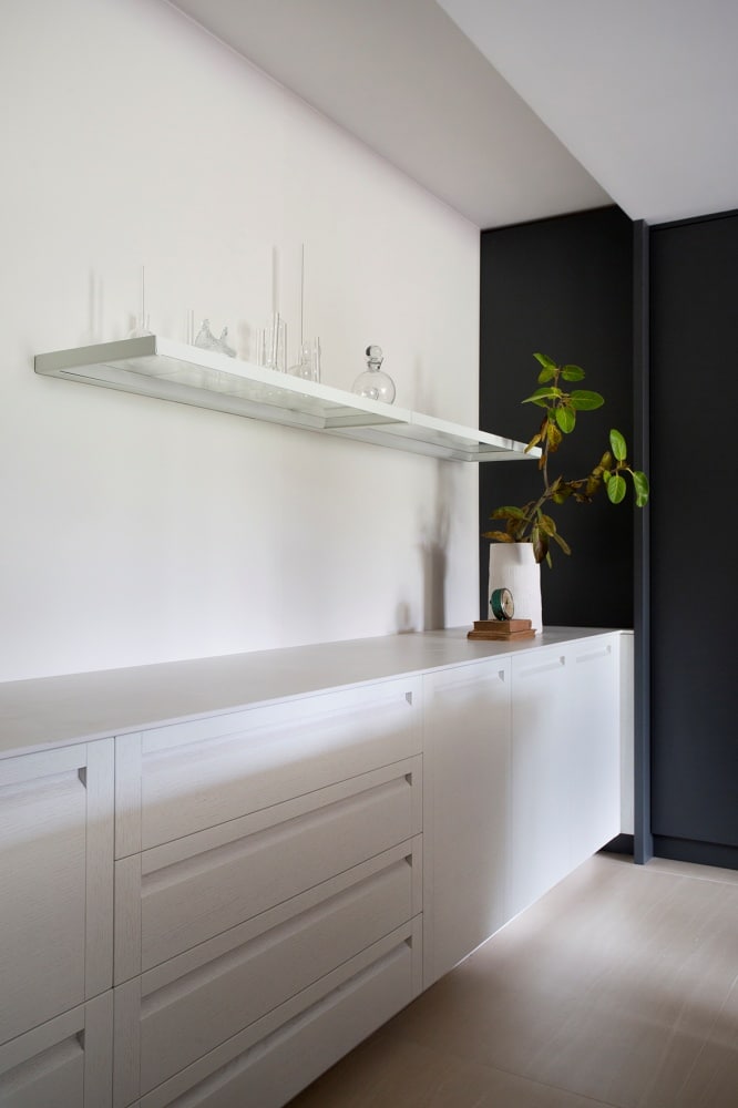 Armário e prateleira branca na cozinha, parede de fundo branca e lateral preta