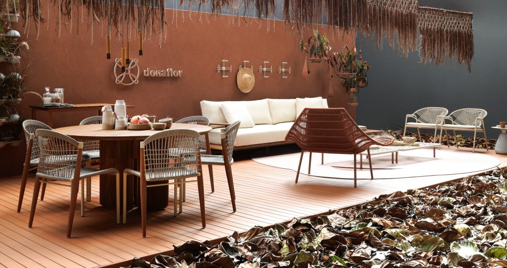 Varanda com piso de deck de madeira, sofás e poltronas brancas, mesas e cadeiras de madeira marrom e parede principal pintada de marrom