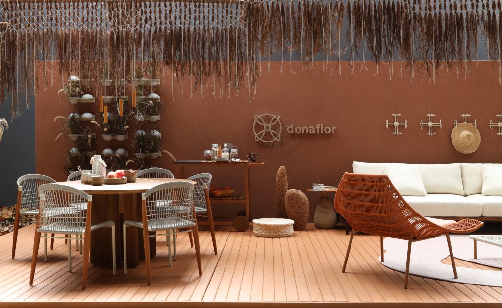 Varanda com piso de deck de madeira, sofás e poltronas brancas, mesas e cadeiras de madeira marrom e parede principal pintada de marrom