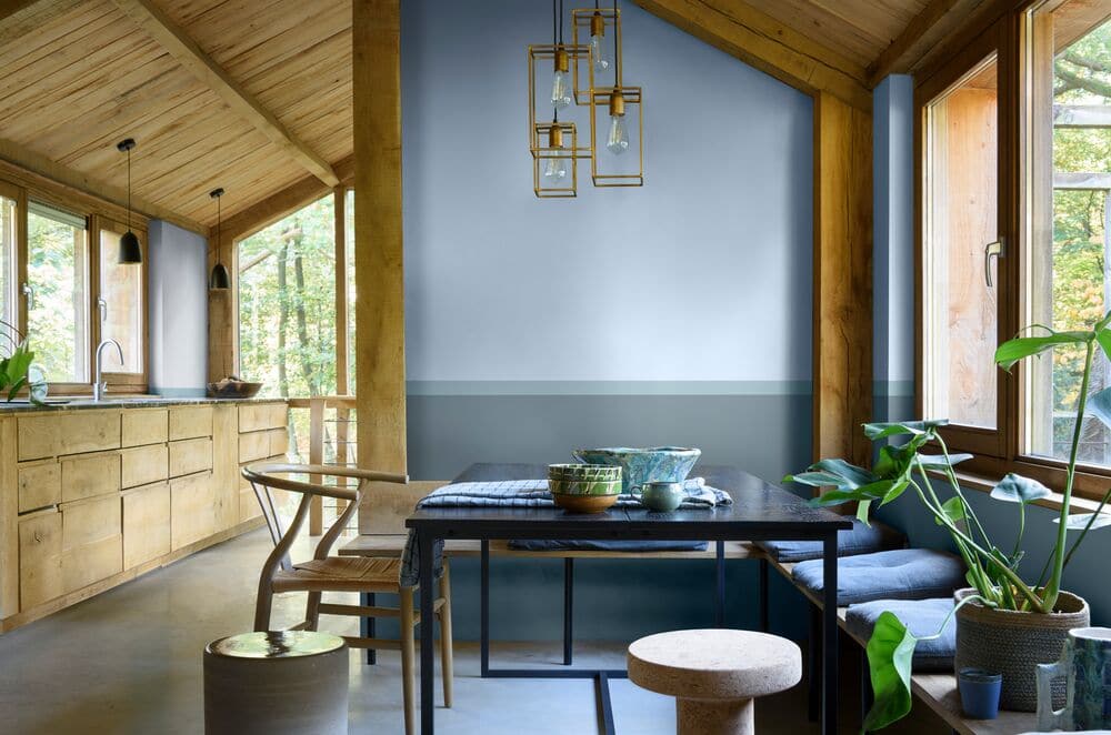 Ambiente com mesa de madeira com sofá estofado azul claro, cadeira de madeira, parede azul claro, teto e armários de madeiro.