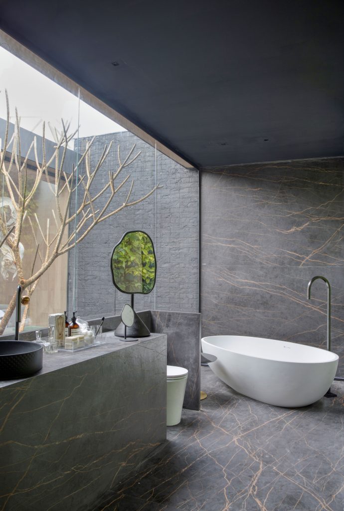 Vidros Vivix: Banheiro com banheira de imersão branca, piso e parede revestido de material marmorizado escuro e parede de vidro
