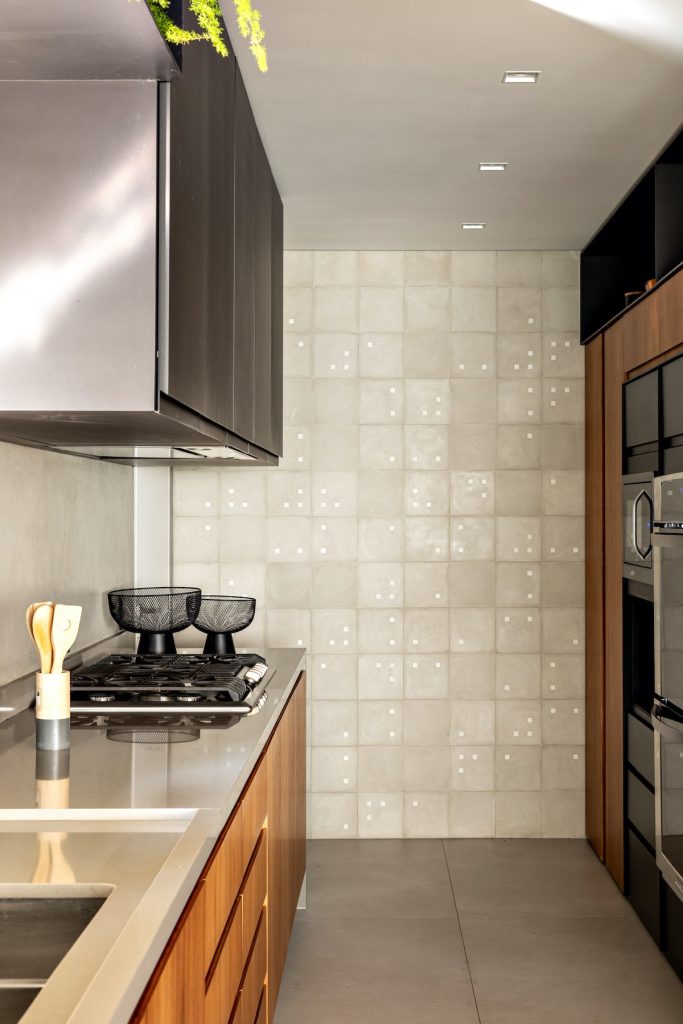 Cozinha pequena com uma parede revestida de ladrilho hidráulico cinza claro, armários amadeirados e cinza, piso em tom cinza