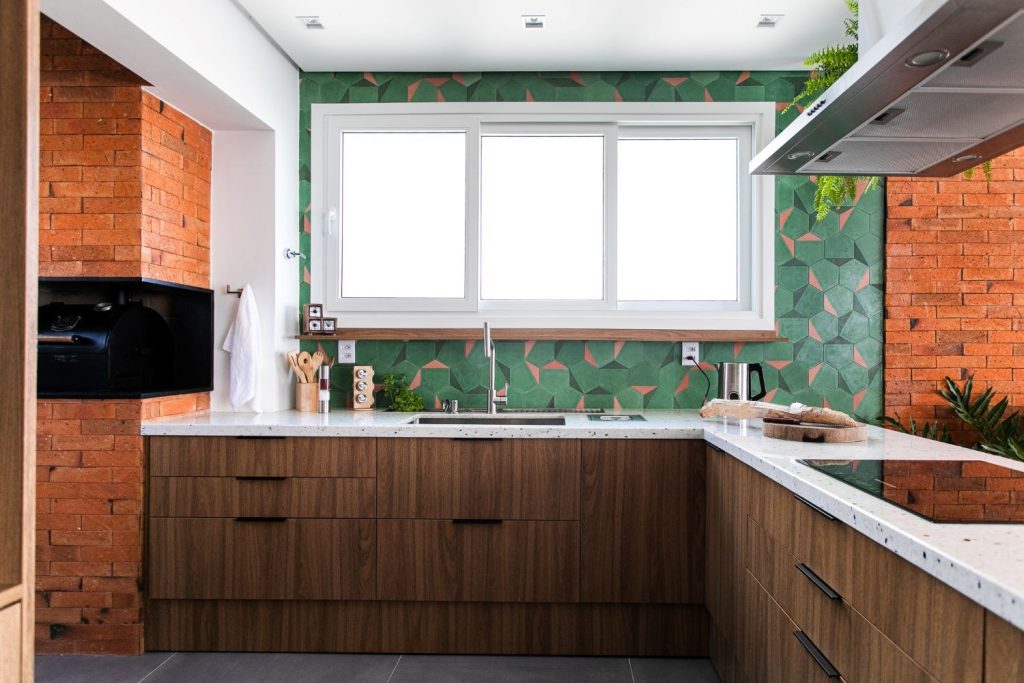 Cozinha com frontão revestido de ladrilho hidráulico verde e laranja, parede de tijolinhos laranja ao redor, armário amadeirado e piso cinza escuro