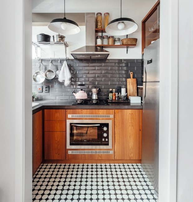 Cozinha com armários de madeira, frontão da pia revestido de subway tiles preto, luminárias pendentes preta e piso de ladrilho hidráulico preto e branco