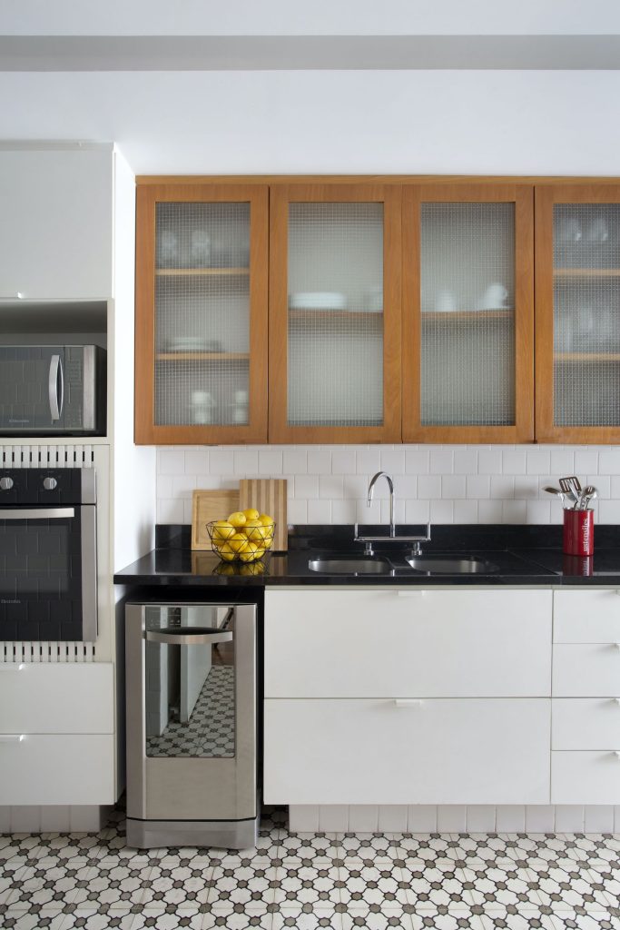Cozinha com armário amadeirado e branco, paredes brancas, piso de ladrilho hidráulico preto e branco 