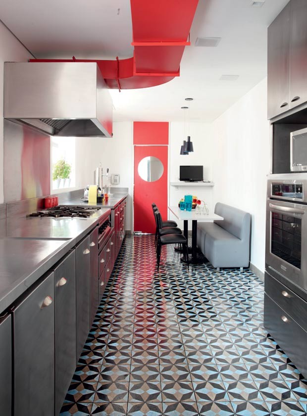 Cozinha com piso ladrilho hidráulico preto e cinza, armários preto e cinza, paredes brancas e detalhe no teto e porta vermelhos.