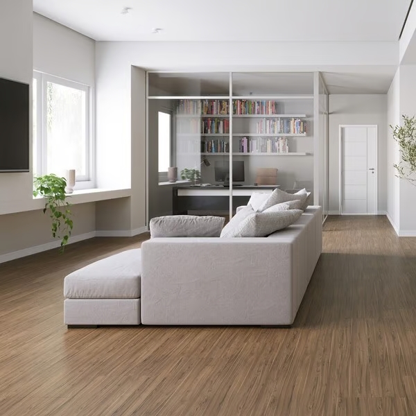 Sala de estar com sofá cinza claro, piso laminado marrom, paredes brancas e vista para escritório com porta de vidro