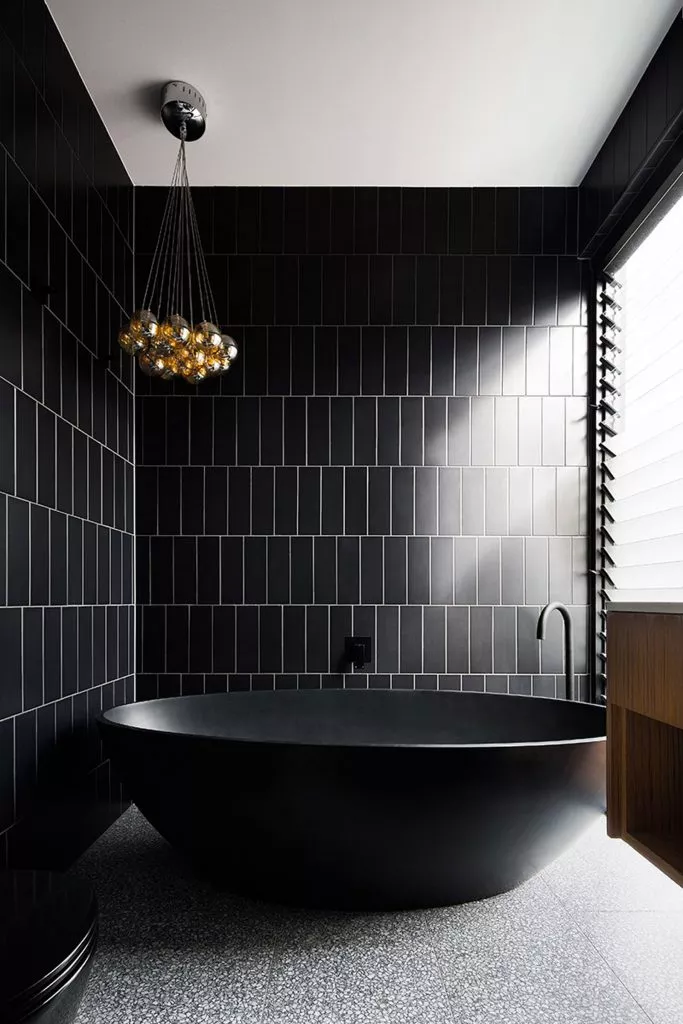 Banheiro com banheira preta, revestimento na parede preto, piso marmorizado cinza e gabinete de madeira