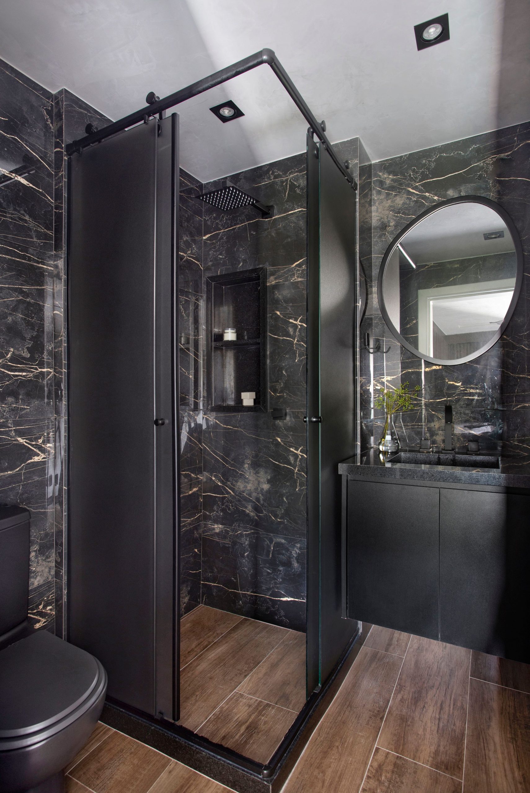 Banheiro com louças e revestimentos da parede preto e piso reproduzindo madeira